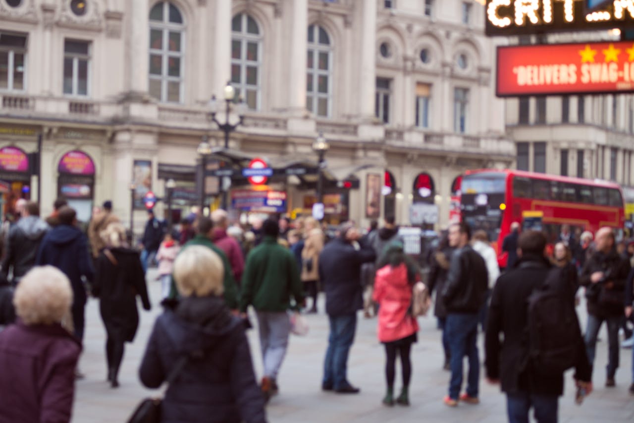Crowd bustling on a London street with iconic red bus and historical buildings.